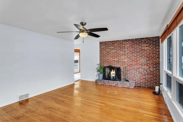 unfurnished living room featuring hardwood / wood-style flooring, brick wall, ceiling fan, and a fireplace