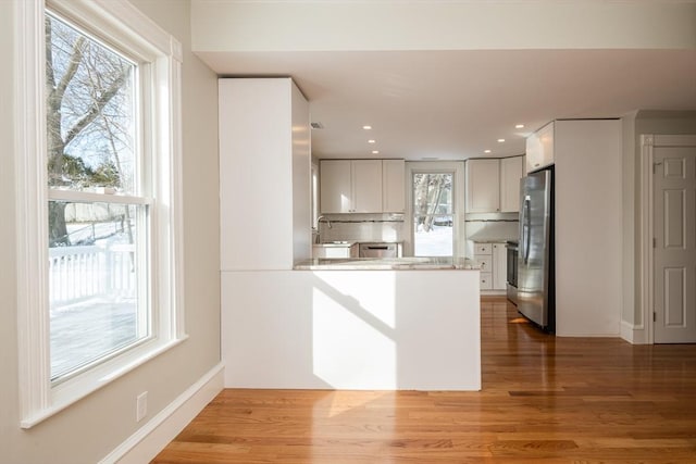 kitchen with backsplash, stainless steel appliances, wood-type flooring, white cabinets, and kitchen peninsula