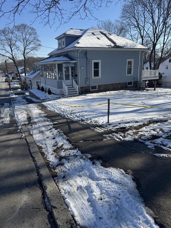 snow covered rear of property featuring a sunroom