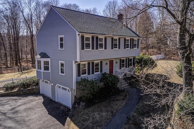 colonial-style house featuring an attached garage, fence, driveway, and a chimney