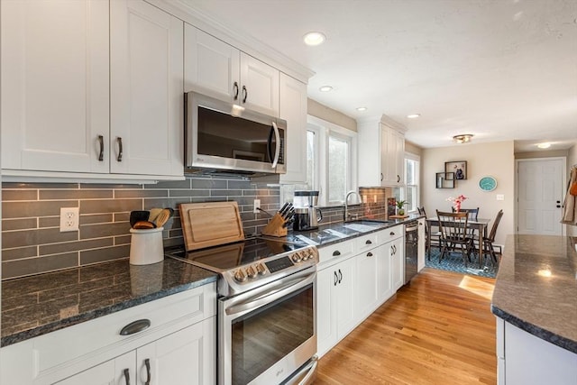 kitchen featuring backsplash, stainless steel appliances, light wood-style floors, white cabinetry, and a sink