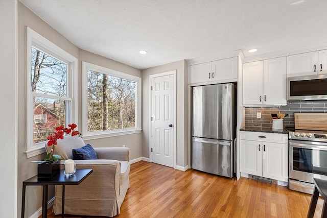 kitchen with baseboards, light wood finished floors, stainless steel appliances, white cabinets, and tasteful backsplash