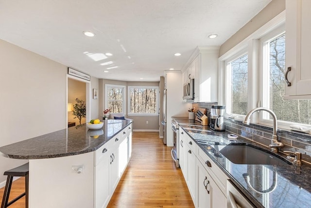 kitchen with light wood-style flooring, a sink, a center island, appliances with stainless steel finishes, and a breakfast bar area