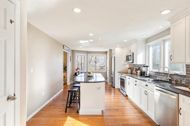 kitchen featuring a breakfast bar area, a sink, appliances with stainless steel finishes, light wood-type flooring, and a center island