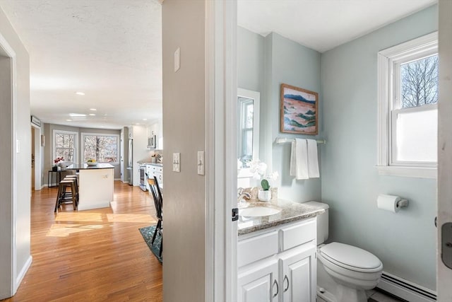 bathroom with baseboards, toilet, baseboard heating, wood finished floors, and vanity