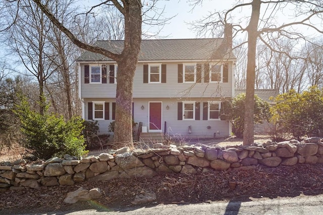 colonial inspired home featuring a shingled roof, entry steps, and a chimney