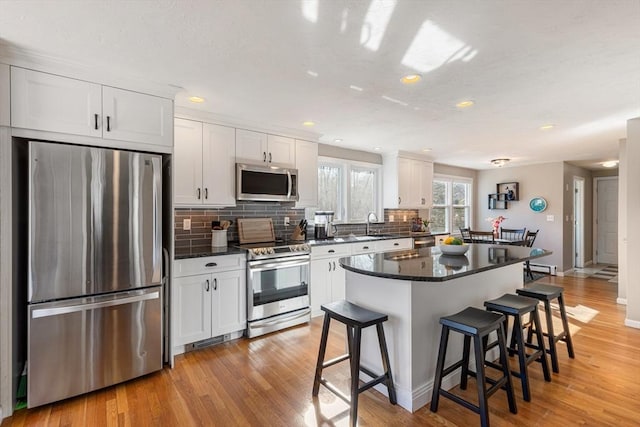 kitchen featuring stainless steel appliances, white cabinets, a kitchen bar, tasteful backsplash, and a center island