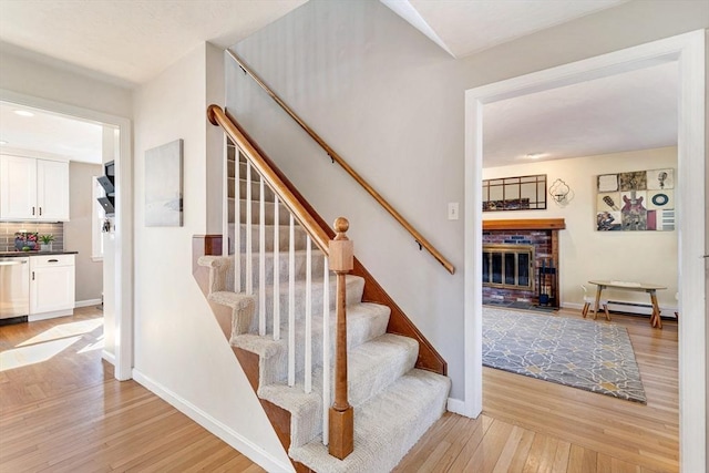 staircase with hardwood / wood-style flooring, a brick fireplace, baseboards, and a baseboard radiator