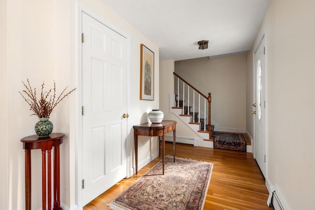 foyer with light wood-type flooring, a baseboard radiator, stairway, and baseboards