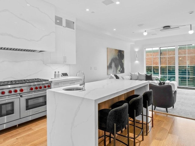 kitchen featuring a sink, double oven range, open floor plan, light wood finished floors, and recessed lighting