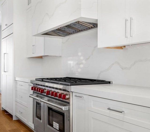 kitchen with double oven range, backsplash, white cabinets, custom range hood, and light wood finished floors