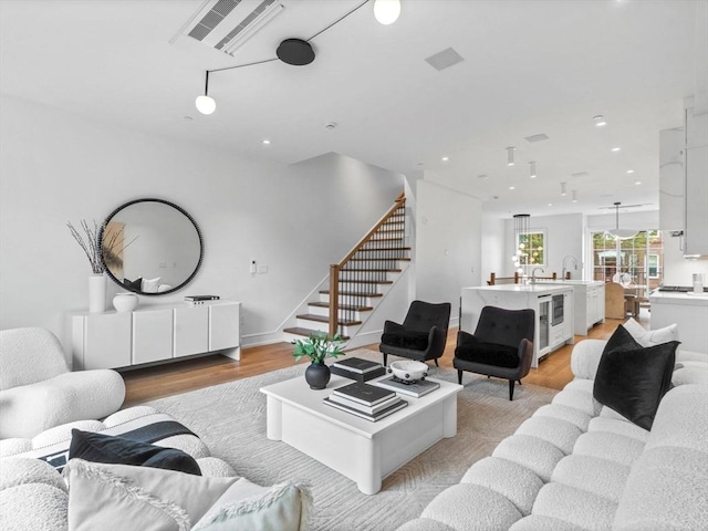 living area with light wood-style flooring, stairs, recessed lighting, and beverage cooler
