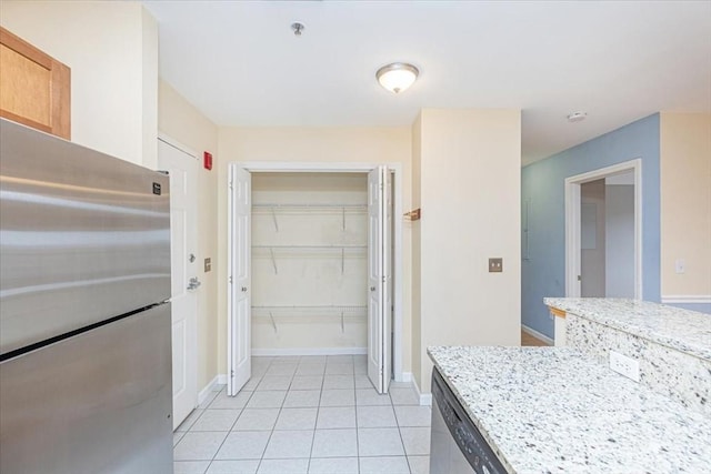 kitchen with light tile patterned flooring, baseboards, appliances with stainless steel finishes, and light stone countertops