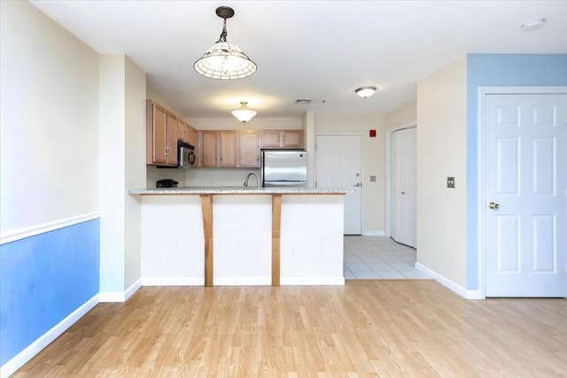 kitchen with stainless steel appliances, a peninsula, light wood-style floors, baseboards, and pendant lighting
