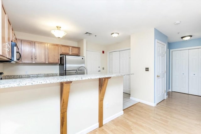 kitchen with stainless steel refrigerator, a peninsula, a kitchen bar, light stone counters, and light wood-type flooring