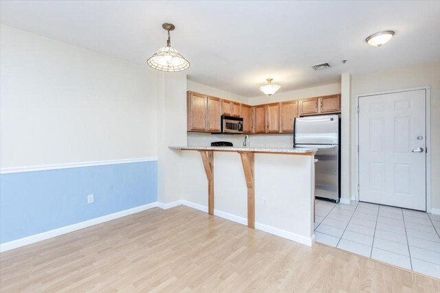 kitchen featuring appliances with stainless steel finishes, light countertops, light wood-style floors, a peninsula, and baseboards