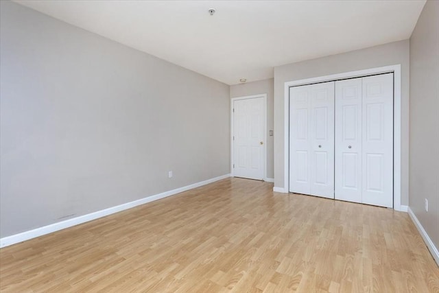 unfurnished bedroom featuring baseboards, light wood finished floors, and a closet