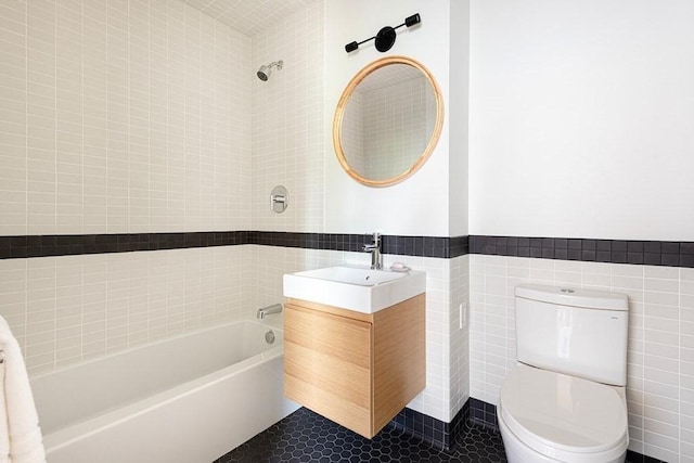 full bathroom with vanity, tile patterned floors, tiled shower / bath combo, toilet, and tile walls