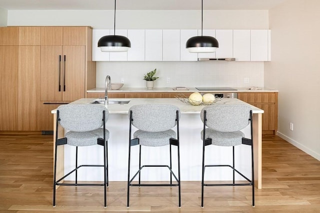 kitchen featuring white cabinetry, sink, pendant lighting, and light hardwood / wood-style floors