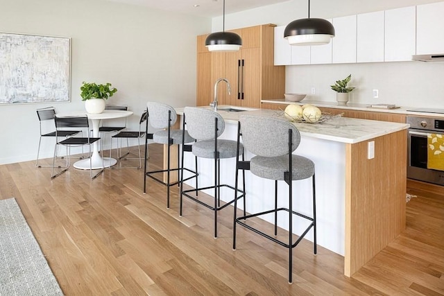 kitchen featuring a center island with sink, oven, white cabinetry, and hanging light fixtures