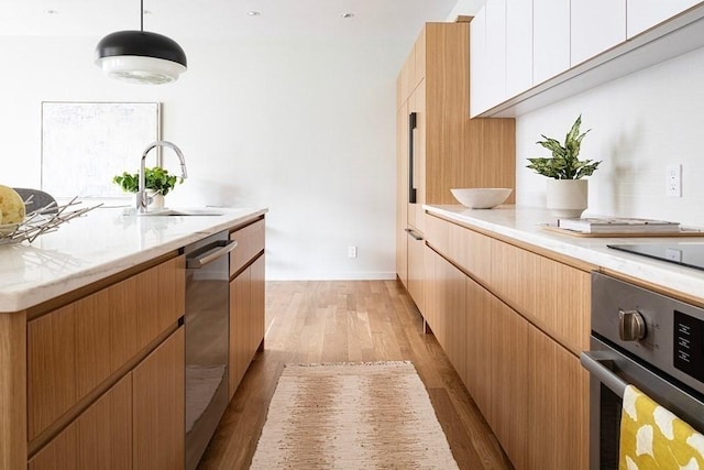 kitchen featuring sink, hanging light fixtures, light hardwood / wood-style floors, white cabinetry, and stainless steel appliances