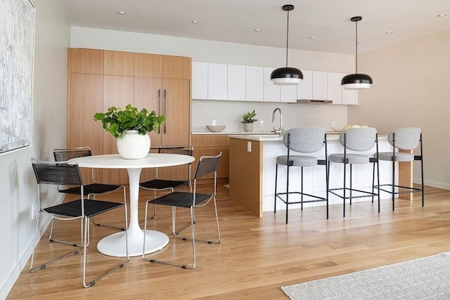 kitchen featuring pendant lighting, light hardwood / wood-style floors, a center island with sink, and white cabinetry