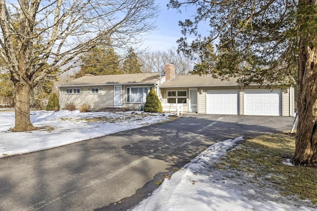 ranch-style home with a garage, a chimney, and aphalt driveway