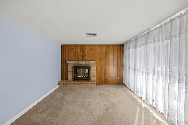 unfurnished living room featuring light carpet, a brick fireplace, baseboards, visible vents, and wood walls