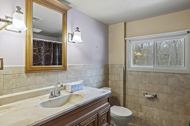 full bath with a wainscoted wall, tile walls, visible vents, toilet, and vanity