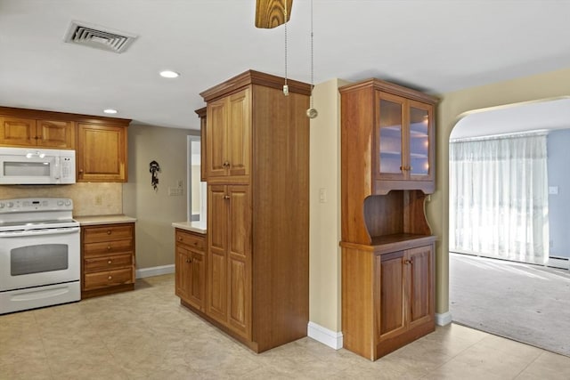 kitchen featuring brown cabinets, light countertops, visible vents, glass insert cabinets, and white appliances