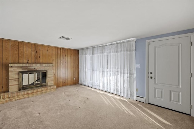 unfurnished living room with light carpet, wood walls, a brick fireplace, and visible vents