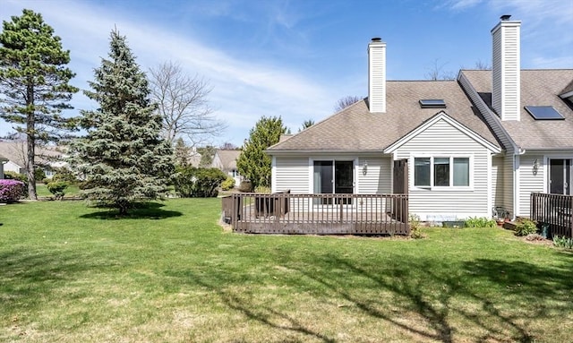 rear view of property featuring a lawn, a wooden deck, a shingled roof, and a chimney