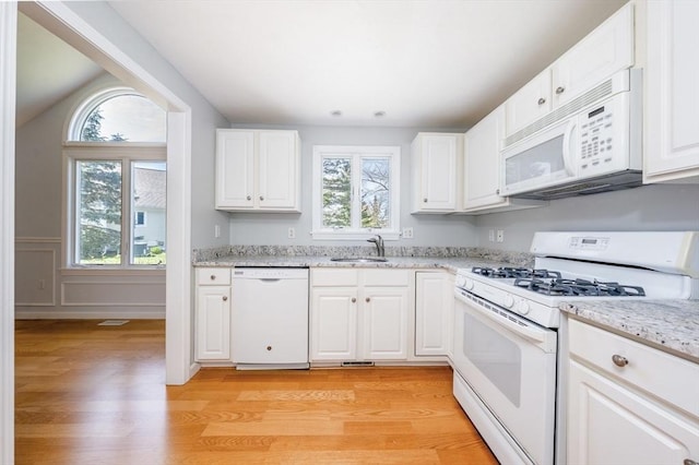 kitchen featuring light wood-style floors, a sink, plenty of natural light, and white appliances