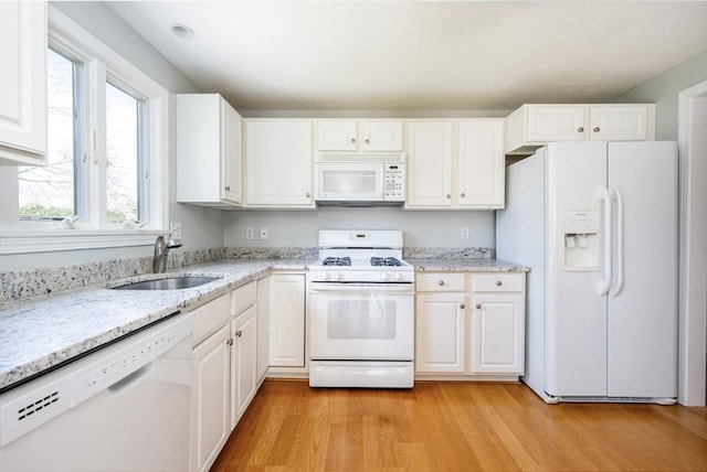kitchen with light wood-type flooring, a sink, light stone counters, white cabinets, and white appliances