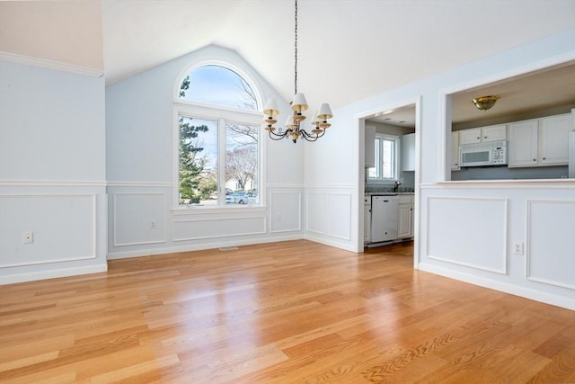 unfurnished dining area with a healthy amount of sunlight, a decorative wall, light wood-style flooring, and a chandelier