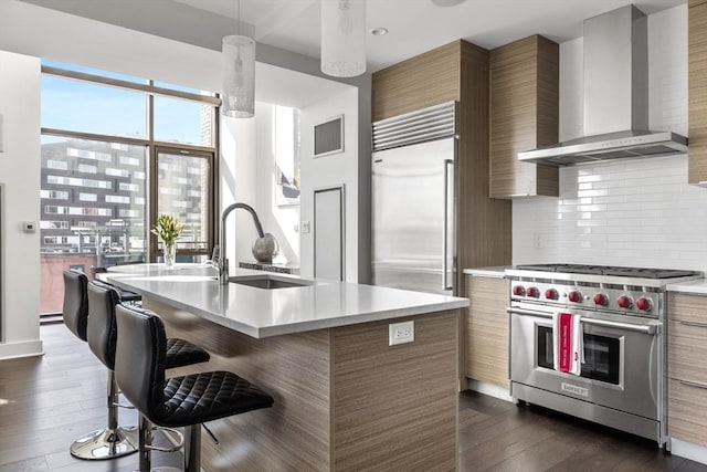 kitchen featuring dark hardwood / wood-style floors, wall chimney range hood, decorative backsplash, high end appliances, and an island with sink