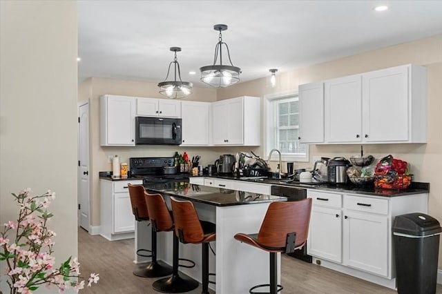 kitchen with a breakfast bar, a sink, white cabinetry, black appliances, and dark countertops