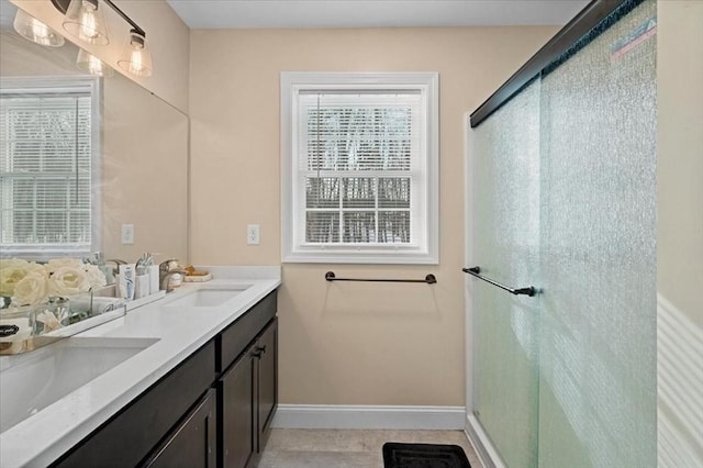 bathroom with double vanity, a shower with door, baseboards, and a sink