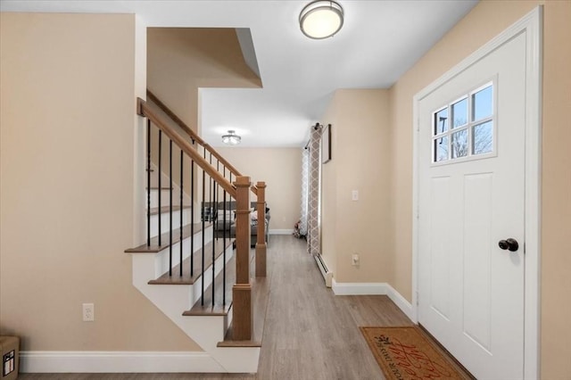 foyer entrance with stairs, baseboard heating, wood finished floors, and baseboards