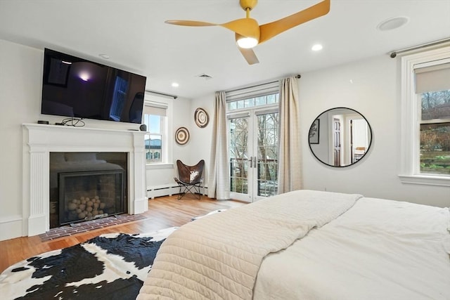 bedroom featuring a fireplace with flush hearth, access to outside, wood finished floors, and multiple windows