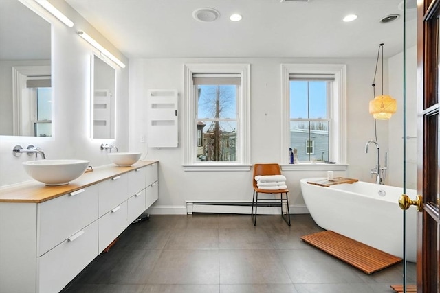 bathroom with a freestanding tub, double vanity, a baseboard heating unit, and a sink