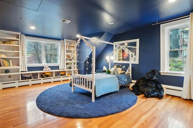 bedroom with a baseboard radiator, wood-type flooring, lofted ceiling, and visible vents