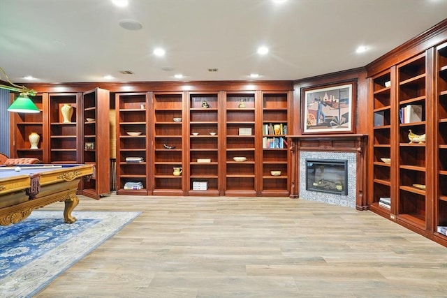 interior space featuring ornamental molding, billiards, recessed lighting, wood finished floors, and a glass covered fireplace