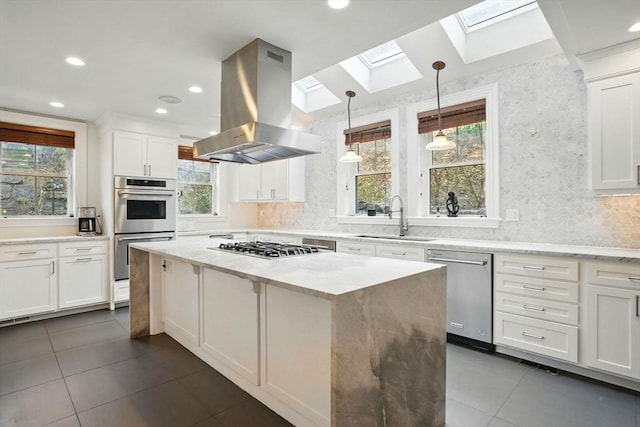 kitchen featuring a sink, appliances with stainless steel finishes, island exhaust hood, a skylight, and a kitchen island
