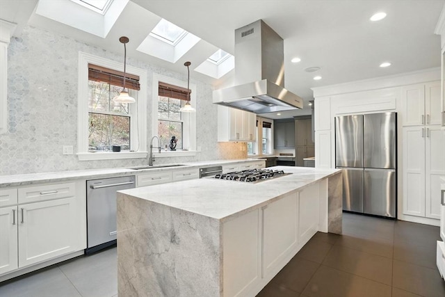 kitchen featuring dark tile patterned flooring, a skylight, island exhaust hood, a sink, and stainless steel appliances