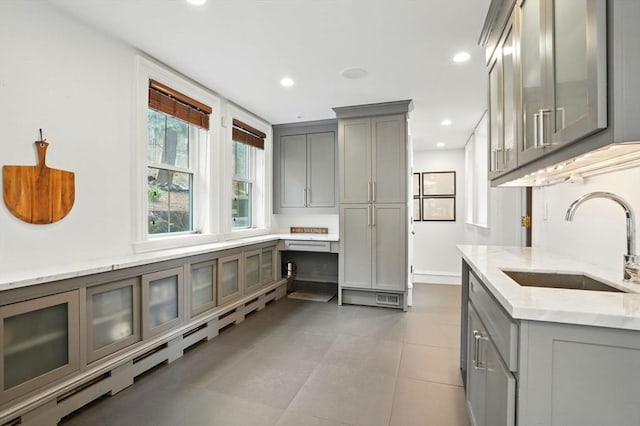 kitchen featuring gray cabinets, light stone counters, a sink, and glass insert cabinets