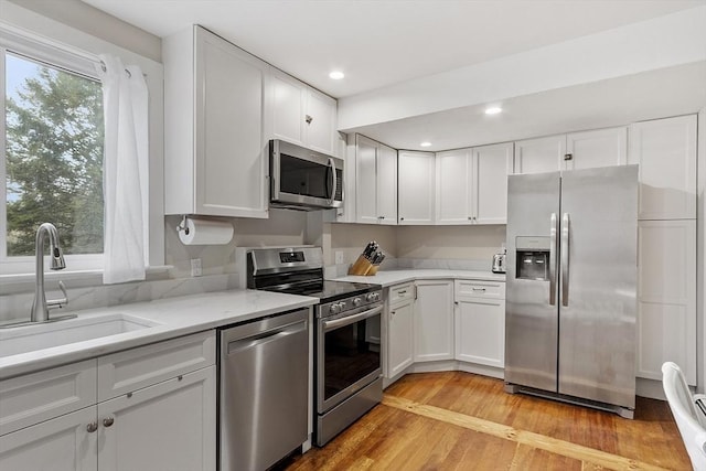 kitchen featuring a sink, appliances with stainless steel finishes, light wood-type flooring, and white cabinetry