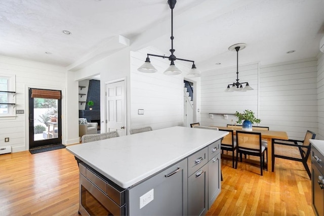 kitchen with gray cabinetry, wood walls, a center island, hanging light fixtures, and light hardwood / wood-style floors