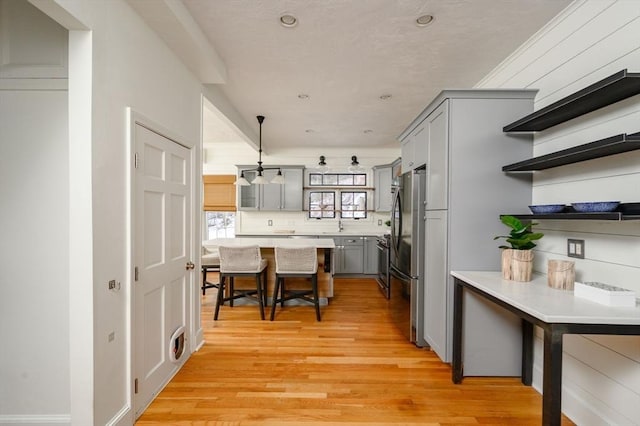 kitchen featuring pendant lighting, gray cabinetry, stainless steel fridge, decorative backsplash, and light hardwood / wood-style flooring