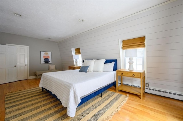 bedroom with hardwood / wood-style floors, wooden walls, and baseboard heating